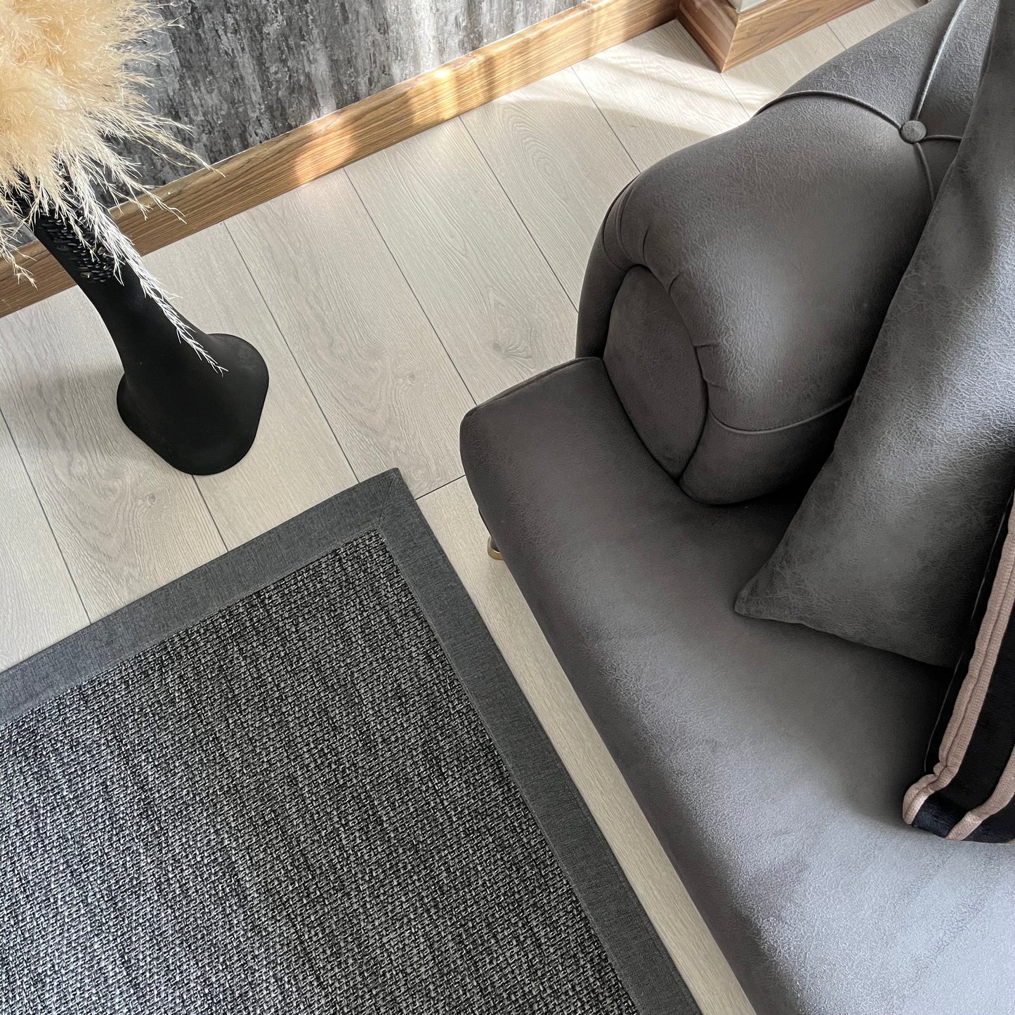 Modern bir oturma odasında gri sisal halı ve koltuk görünümü, şık bir dekorasyon önerisi.