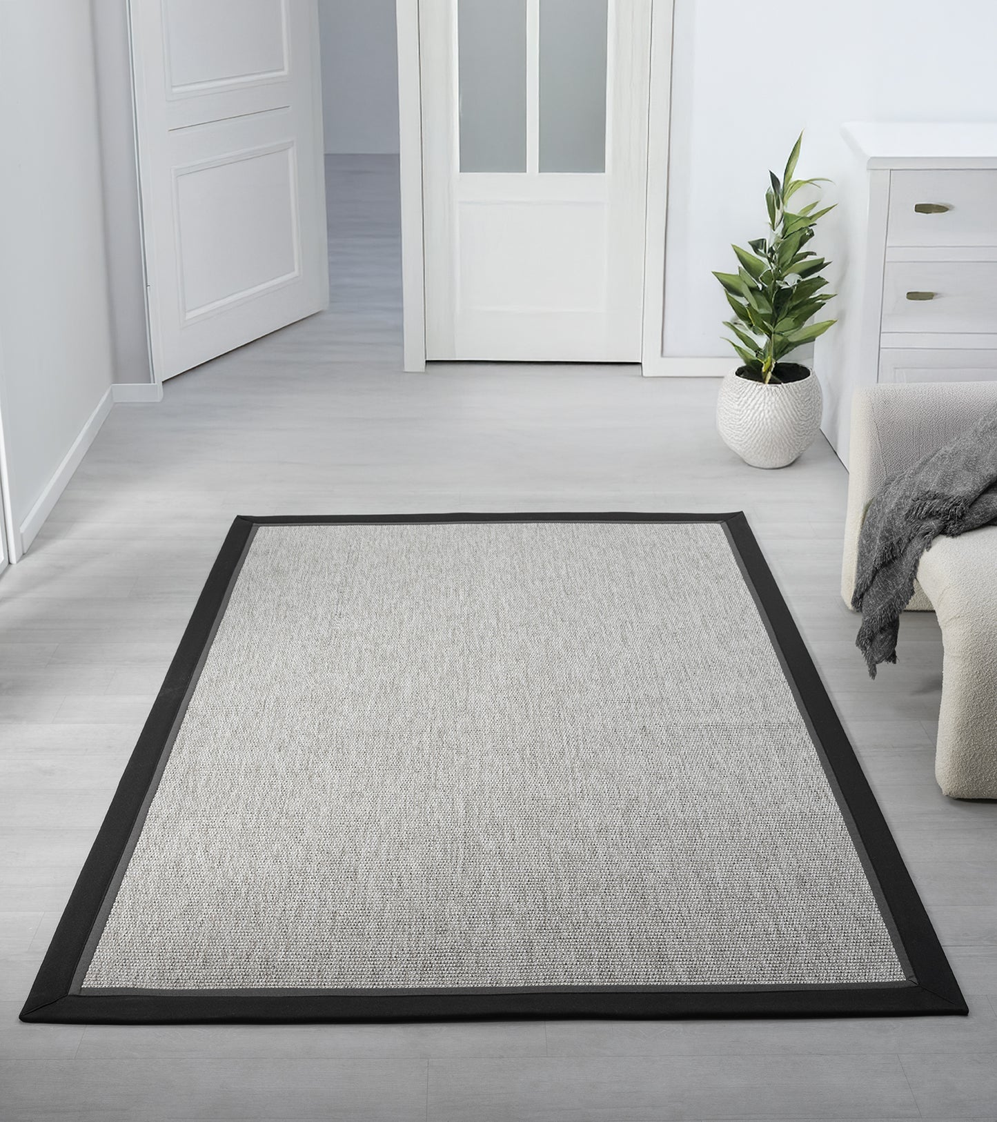 Aydınlık bir odaya yerleştirilmiş gri kumaş bordürlü sisal halı, yerin ahşap kaplamasıyla uyumlu ve minimalist bir görünüm sunuyor.
