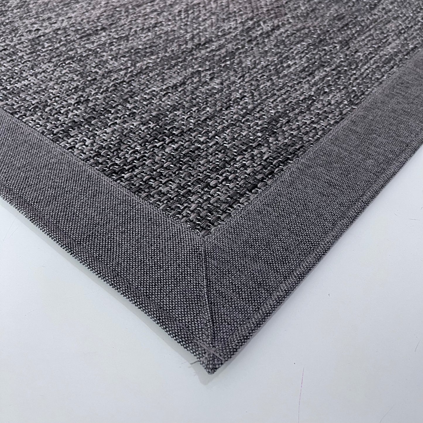 Gri sisal halının detaylı bir görüntüsü, kenarında kumaş bordürü ile modern bir görünüm sunuyor.