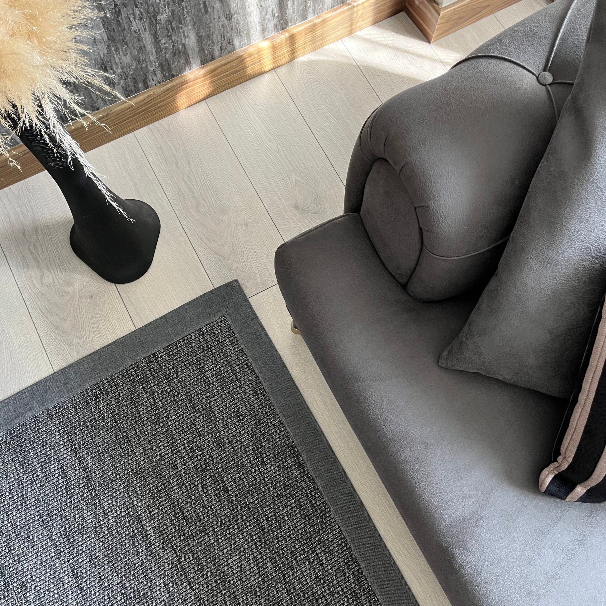 Modern bir oturma odasında gri sisal halı ve koltuk görünümü, şık bir dekorasyon önerisi.