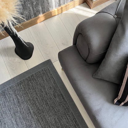 Modern bir oturma odasında gri sisal halı ve koltuk görünümü, şık bir dekorasyon önerisi.