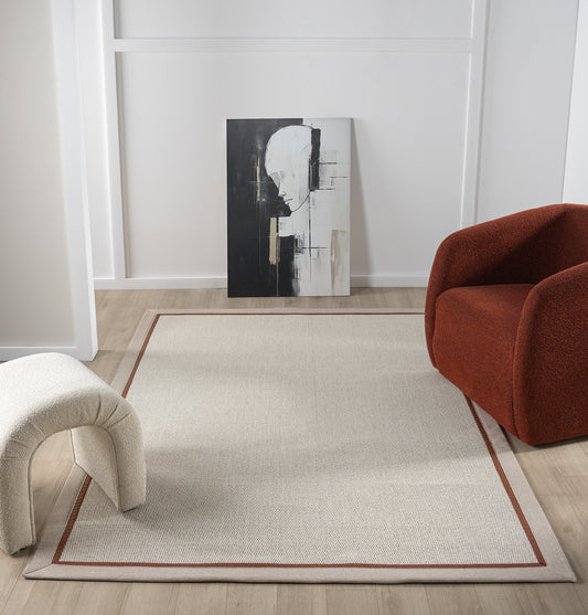 Şık bir oturma odasında yer alan krem rengi balık sırtı desenli el yapımı sisal halı. Halının etrafında modern bir koltuk ve bir sanat eseri bulunuyor.