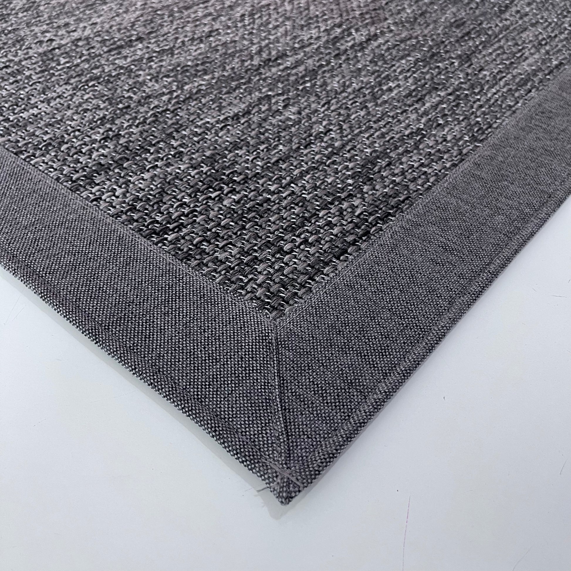 Gri sisal halının detaylı bir görüntüsü, kenarında kumaş bordürü ile modern bir görünüm sunuyor.