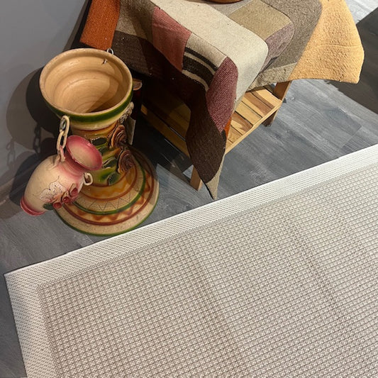 Krem rengi jüt sisal halının kenarında, desenli bir örtü ile birlikte dekoratif bir çömlek yer alıyor.