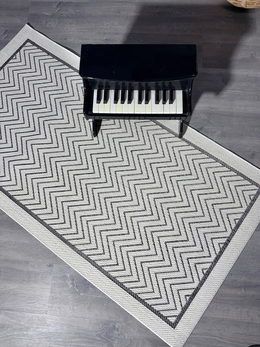 Halı Vagonu JS9718 jüt sisal halı, zigzag desenli antrasit beyaz. Halının üstünde küçük bir piyano yer alıyor.