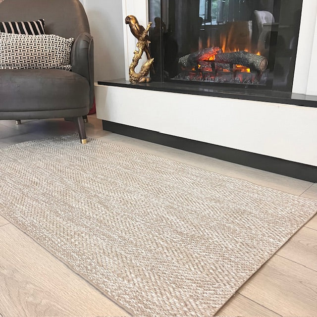 Sisal halı, modern bir şalı oturma alanına estetik katıyor. Arkada dekoratif bir şömine görülüyor.
